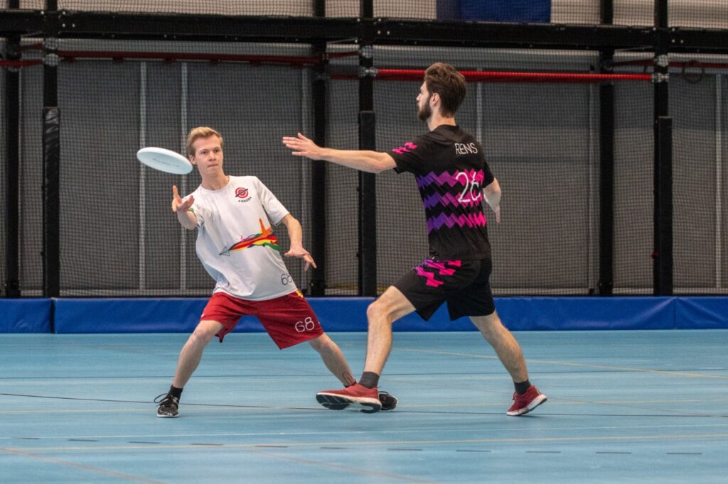 2 ultimate frisbeeers, de linker in Airborn-shirt gooit de schijf, de ander probeert die tegen te houden